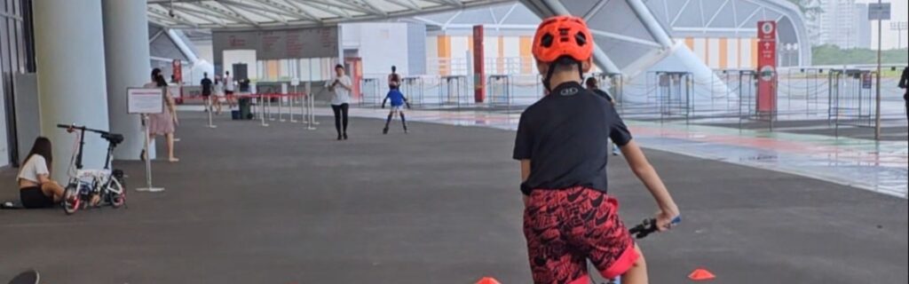 A child in an orange helmet riding through a line of cones under the National Stadium roof