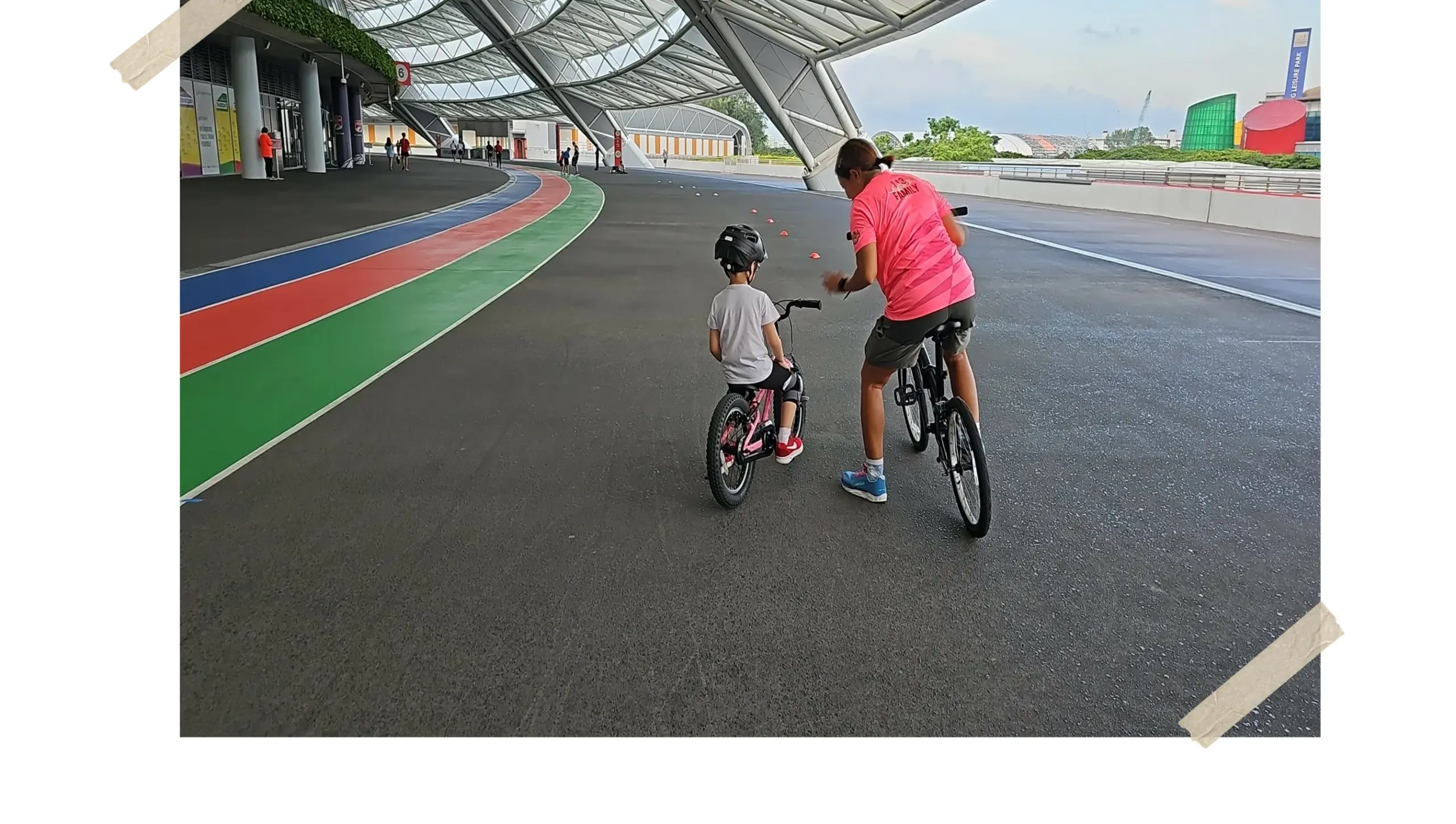 A Saddlewerkz coach riding beside a small helmeted learner through a cone drill under the National Stadium roof, a taped-in print on the lesson record
