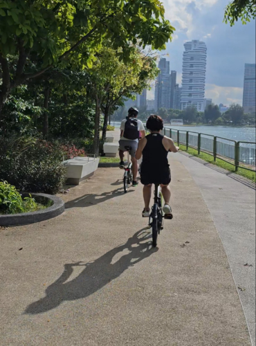 Two adults riding a waterfront path with the city skyline behind them